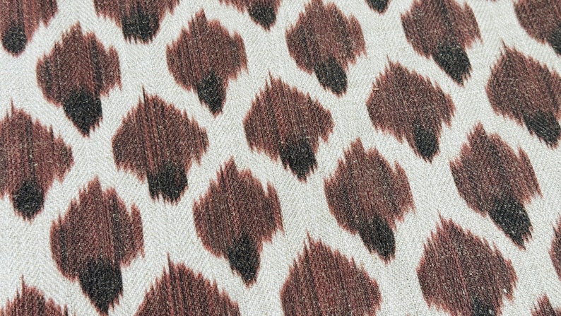 May include: Close-up of a white fabric with a brown and black animal print pattern. The pattern resembles a leopard print.
