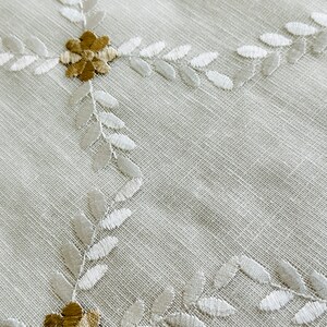May include: White fabric with a delicate embroidered pattern of leaves and flowers in shades of white and brown.