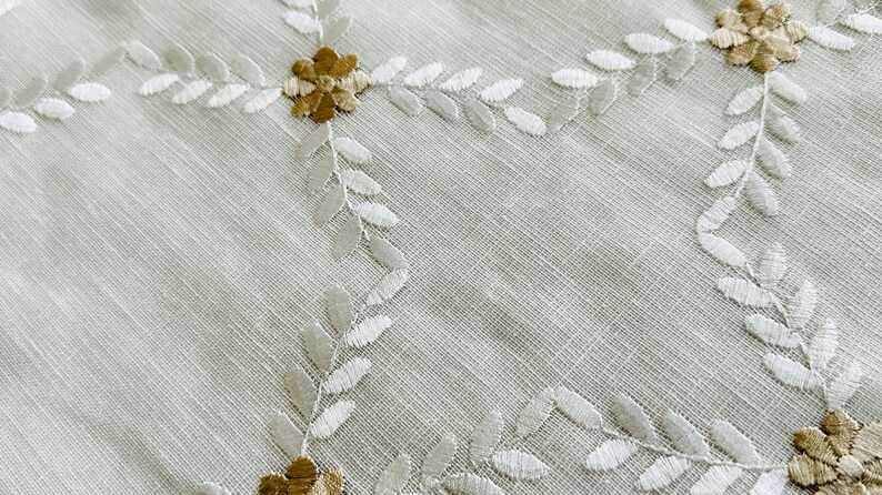 May include: White fabric with a delicate embroidered pattern of leaves and flowers in shades of white and brown.
