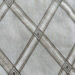 May include: A white fabric with a criss-cross pattern of brown and white embroidered lines. The lines form diamond shapes.