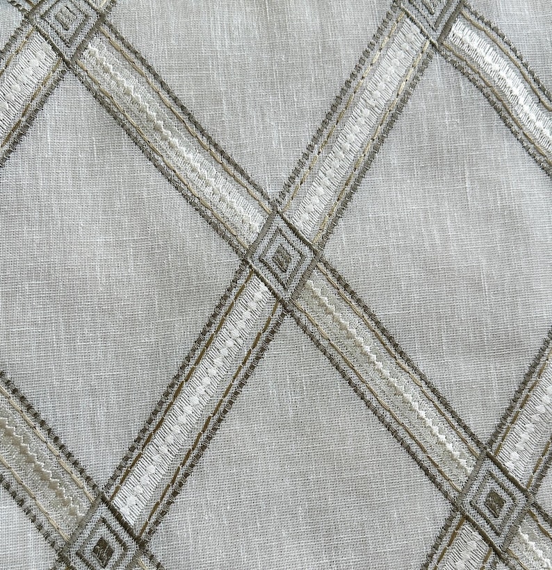 May include: A white fabric with a criss-cross pattern of brown and white embroidered lines. The lines form diamond shapes.