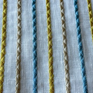 May include: Close-up of a white fabric with woven stripes in blue, yellow, and beige.