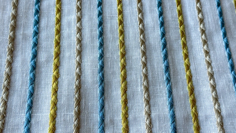 May include: Close-up of a white fabric with woven stripes in blue, yellow, and beige.
