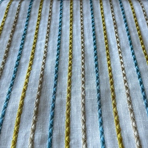 May include: White fabric with embroidered stripes in yellow, blue, and beige.