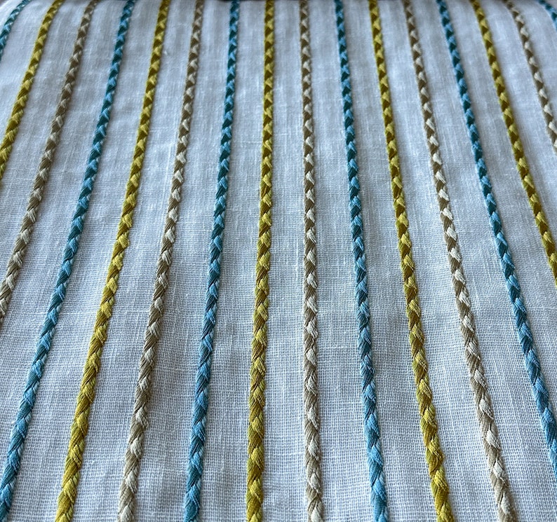 May include: White fabric with embroidered stripes in yellow, blue, and beige.
