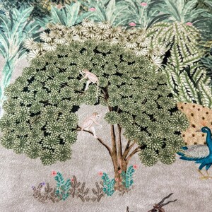 K&ouml;nnte beinhalten: Ein beigefarbener Stoff mit einem gestickten Design eines gr&uuml;nen Baumes mit zwei Affen, einem blauen Vogel und einem Pfau. Der Hintergrund ist hellbeige mit gr&uuml;nem Laub.