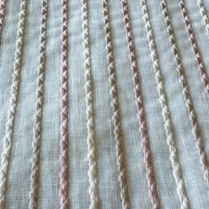 Puede incluir: Primer plano de una tela blanca con rayas verticales de hilo trenzado beige y rosa.