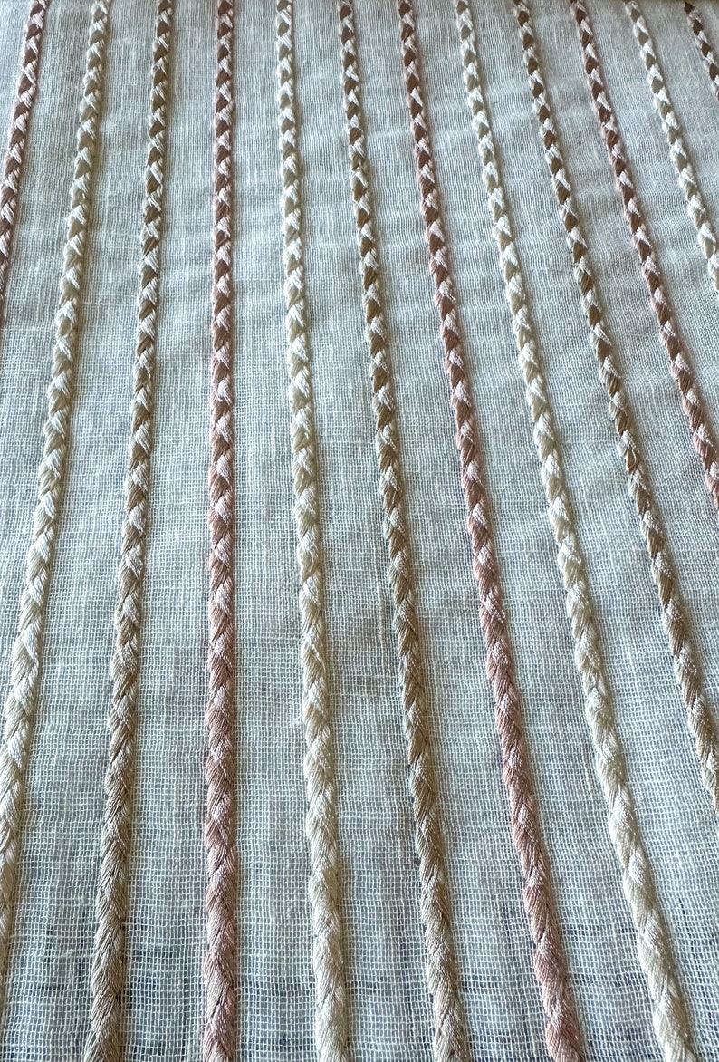 Puede incluir: Primer plano de una tela blanca con rayas verticales de hilo trenzado beige y rosa.