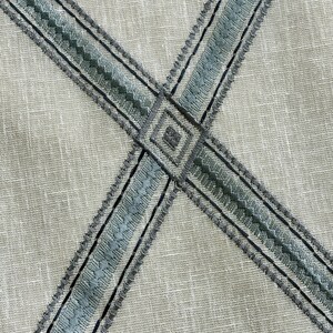 K&ouml;nnte beinhalten: Nahaufnahme eines beigefarbenen Stoffes mit einem Kreuzmuster aus blauem und schwarzem Stickband.