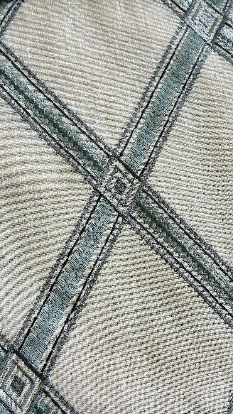 K&ouml;nnte beinhalten: Nahaufnahme eines beigefarbenen Stoffes mit einem Kreuzmuster aus blauem und schwarzem Stickband.