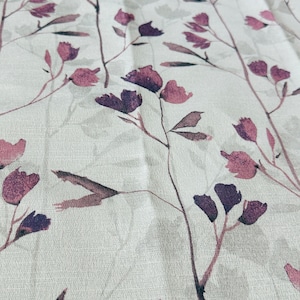 May include: A white fabric with a subtle texture featuring a repeating pattern of delicate purple and gray floral sprigs.