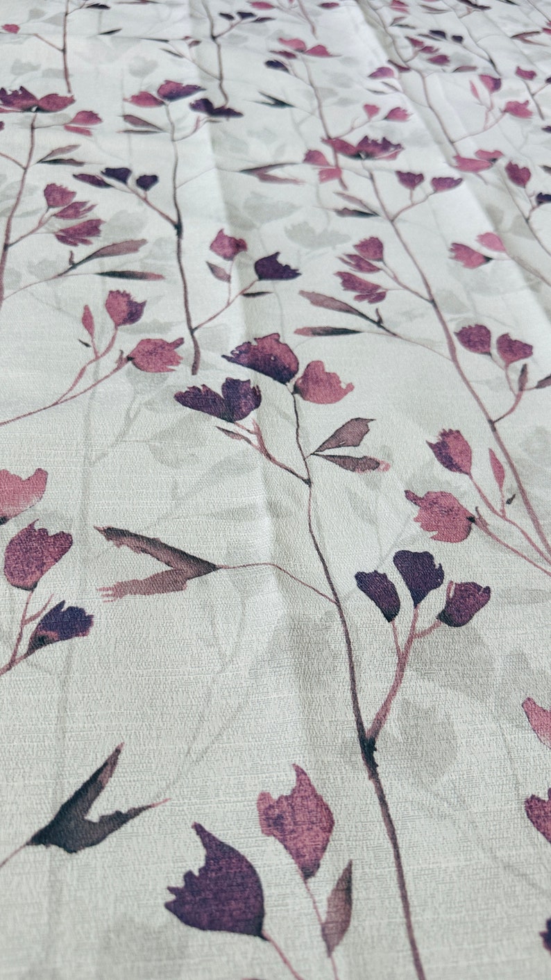 May include: A white fabric with a subtle texture featuring a repeating pattern of delicate purple and gray floral sprigs.