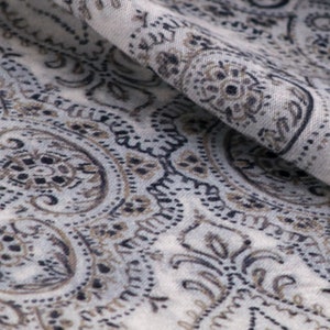 May include: Close-up of a white fabric with a paisley pattern in shades of brown and black.