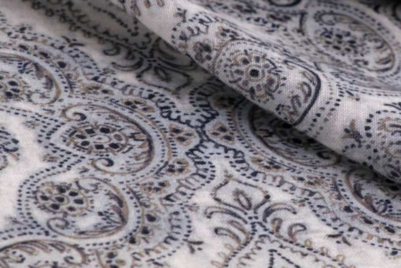 May include: Close-up of a white fabric with a paisley pattern in shades of brown and black.