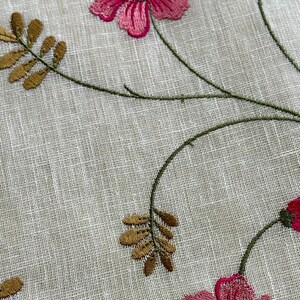 May include: Embroidered floral fabric with pink flowers and green stems on a white linen background.
