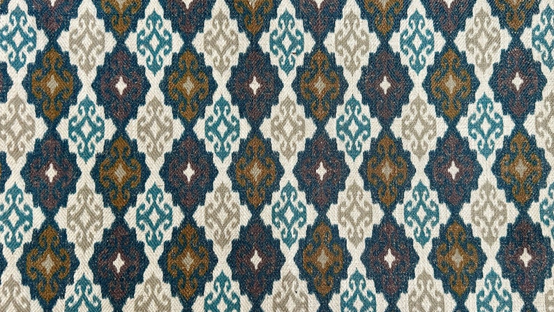 May include: A fabric with a repeating geometric pattern in shades of blue, brown, and beige. The pattern features a diamond shape with a stylized floral design inside.