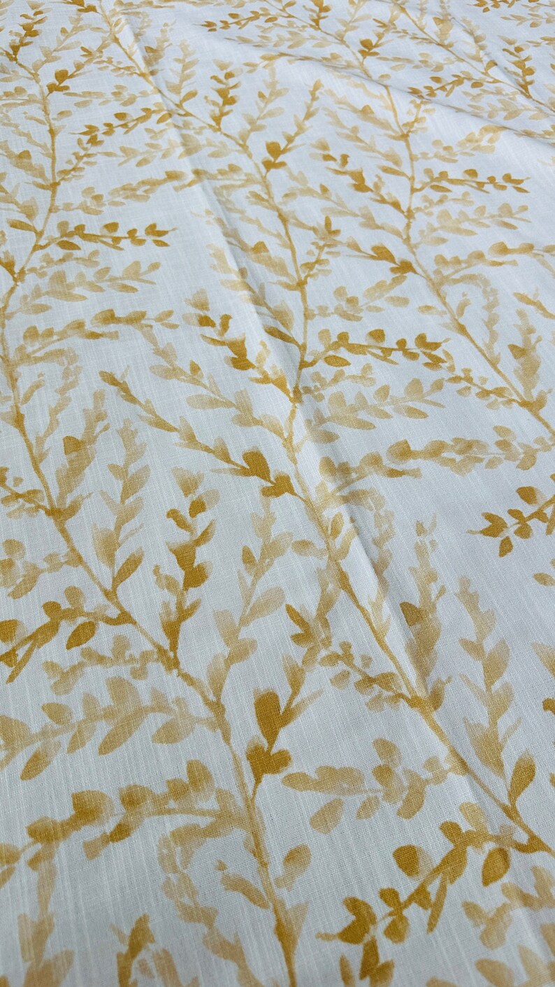 May include: White fabric with a subtle linen texture featuring a repeating pattern of gold-colored leafy branches.