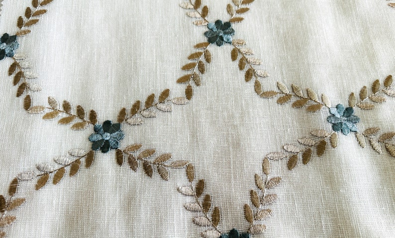Puede incluir: Tela blanca con un patr&oacute;n bordado de hojas marrones y flores azul verdoso.