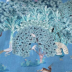 May include: A blue fabric with a repeating pattern of a peacock, monkeys, a deer, and a bird. The background is a light blue colour.