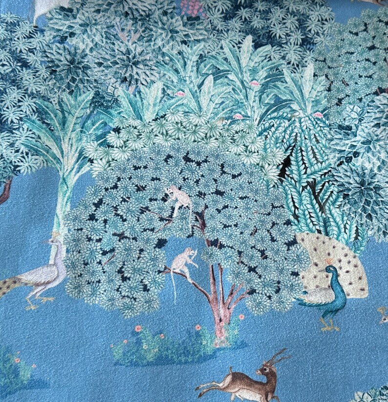 May include: A blue fabric with a repeating pattern of a peacock, monkeys, a deer, and a bird. The background is a light blue colour.