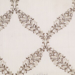 May include: White fabric with a repeating pattern of brown embroidered floral designs. The design is a series of connected ovals with a floral pattern.