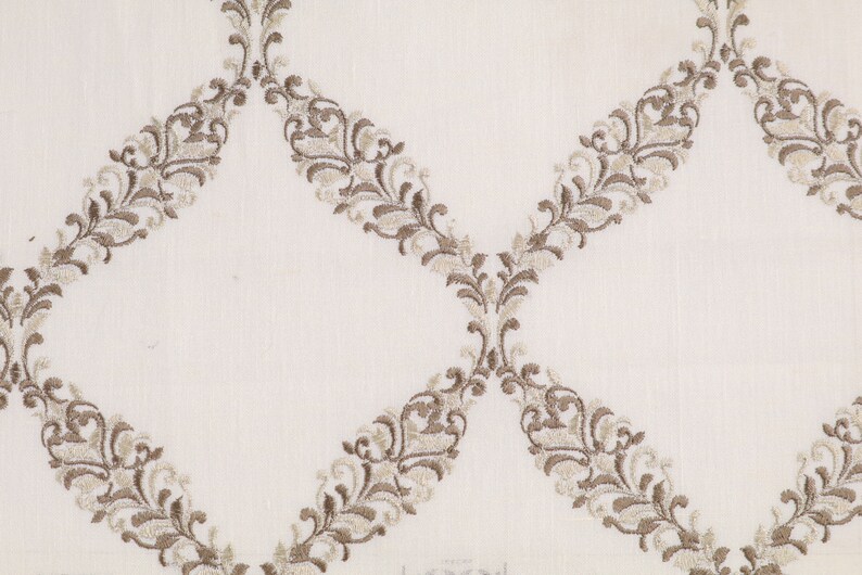 May include: White fabric with a repeating pattern of brown embroidered floral designs. The design is a series of connected ovals with a floral pattern.