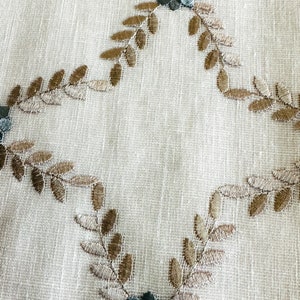 Puede incluir: Tela blanca con hojas bordadas marrones y flores azules.