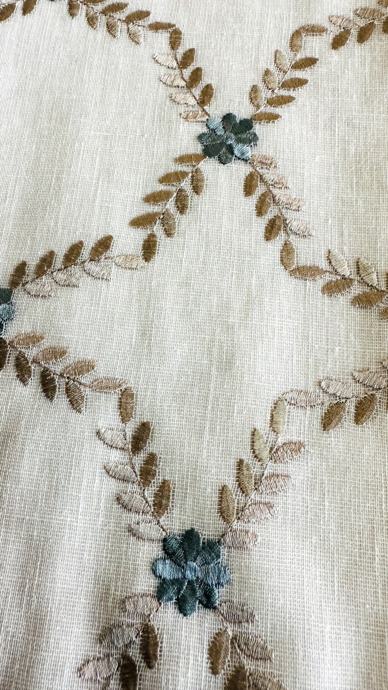 Puede incluir: Tela blanca con hojas bordadas marrones y flores azules.