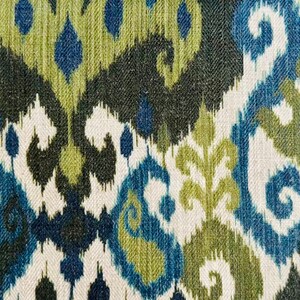 May include: Textile with an ikat pattern in shades of blue, green, and white. The design features stylized floral and paisley motifs, creating a textured, decorative surface. The fabric has a woven appearance, suitable for upholstery or home decor.