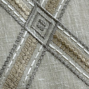 May include: Close-up of a white fabric with a criss-cross pattern of gray and beige embroidery.