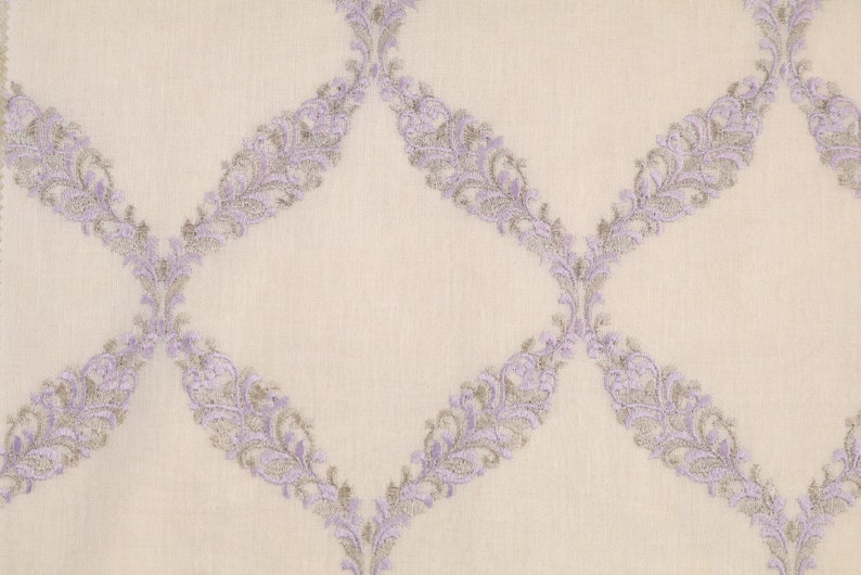May include: A white fabric with a repeating pattern of lavender and gray floral designs. The design is a diamond shape with a floral pattern on each side.