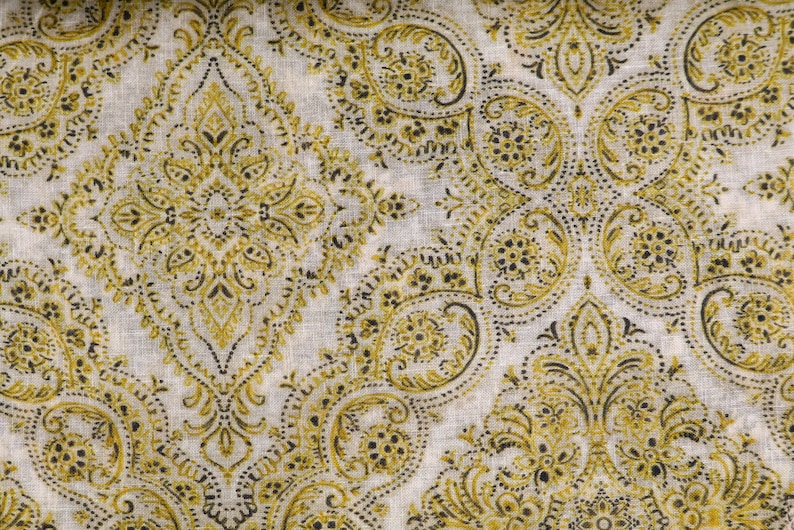 May include: A white fabric with a repeating pattern of gold and black paisley designs. The fabric has a subtle texture.