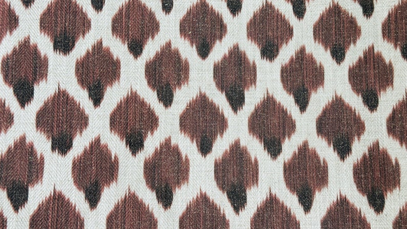May include: A white fabric with a brown and black ikat pattern. The pattern is a repeating diamond shape with a brown center and black edges.