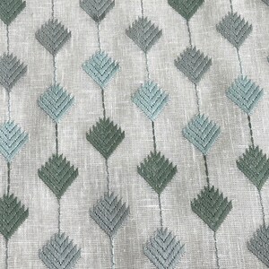 May include: White fabric with a repeating pattern of blue and green embroidered diamond shapes. The diamonds are made up of a series of small, overlapping triangles.