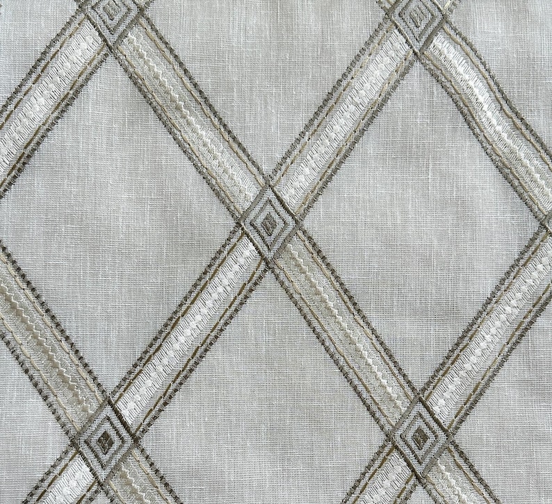 May include: A close-up of a beige fabric with a diamond pattern woven into the fabric. The diamond pattern is made of a thin, white thread and a thicker, brown thread.