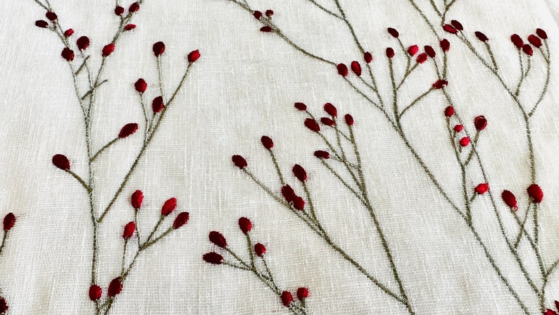 K&ouml;nnte beinhalten: Wei&szlig;er Stoff mit gestickten roten Beeren und gr&uuml;nen Stielen. Der Stoff hat eine subtile Textur.