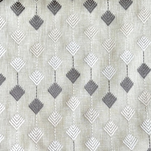May include: Close-up of a fabric with a repeating diamond pattern. The diamonds are embroidered in alternating shades of gray and white, connected by vertical lines. The background is a light beige color, giving the fabric a textured appearance.
