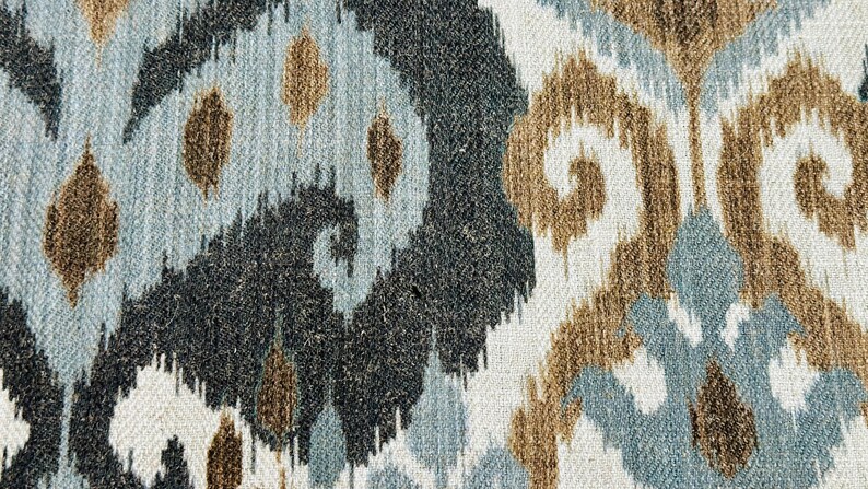 Puede incluir: Primer plano de una tela con un patr&oacute;n ikat marr&oacute;n, azul y blanco. La tela tiene una superficie texturizada y un patr&oacute;n repetitivo de remolinos y puntos.