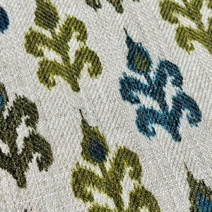 May include: Close-up of a fabric with a repeating pattern of stylized green and blue leaves on a white background.