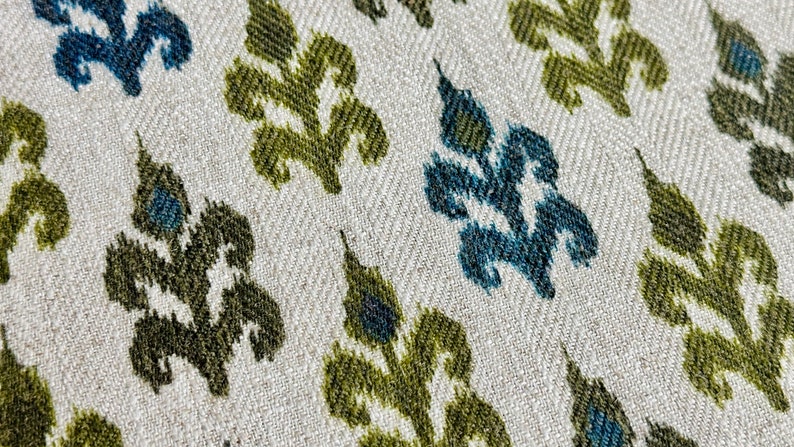 May include: Close-up of a fabric with a repeating pattern of stylized green and blue leaves on a white background.
