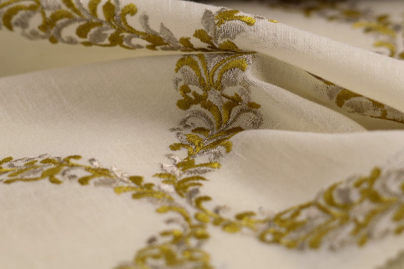 May include: White fabric with a repeating pattern of gold and silver embroidered floral designs.