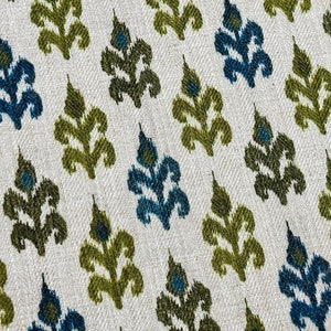 May include: A white fabric with a repeating pattern of green and blue stylized leaves. The fabric has a subtle herringbone weave.