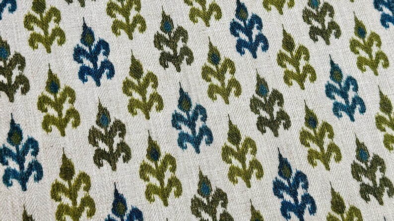 May include: A white fabric with a repeating pattern of green and blue stylized leaves. The fabric has a subtle herringbone weave.