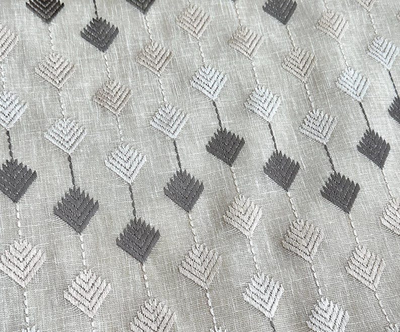 May include: Close-up of a fabric with a repeating pattern of diamond shapes. The diamonds are in shades of gray and beige, connected by thin lines. The fabric has a textured appearance, suggesting a linen or similar material.