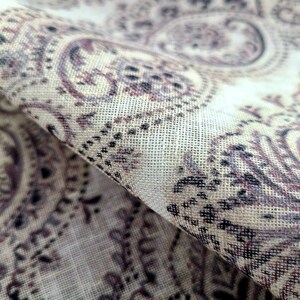 May include: Close-up of a beige fabric with a paisley pattern in shades of brown and black. The fabric has a textured, woven look.