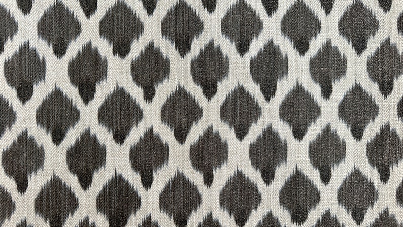 May include: A white fabric with a black ikat pattern. The pattern is a repeating diamond shape with a small, pointed center.