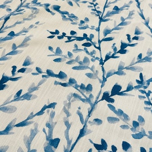 May include: Close-up of a fabric with a repeating pattern of blue watercolor-style branches and leaves against a cream-colored background. The design has a natural, botanical theme, suitable for home decor.