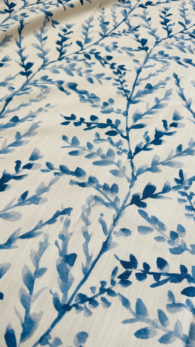 May include: Close-up of a fabric with a repeating pattern of blue watercolor-style branches and leaves against a cream-colored background. The design has a natural, botanical theme, suitable for home decor.