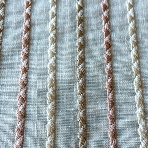 Puede incluir: Primer plano de una tela blanca con rayas verticales de hilo trenzado beige y rosa claro.