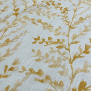 May include: White fabric with a subtle texture featuring a repeating pattern of gold-colored leafy branches.